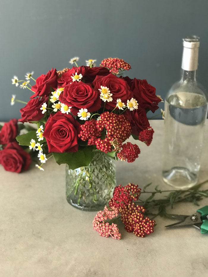 a small bouquet of red roses, daisies, and yarrow
