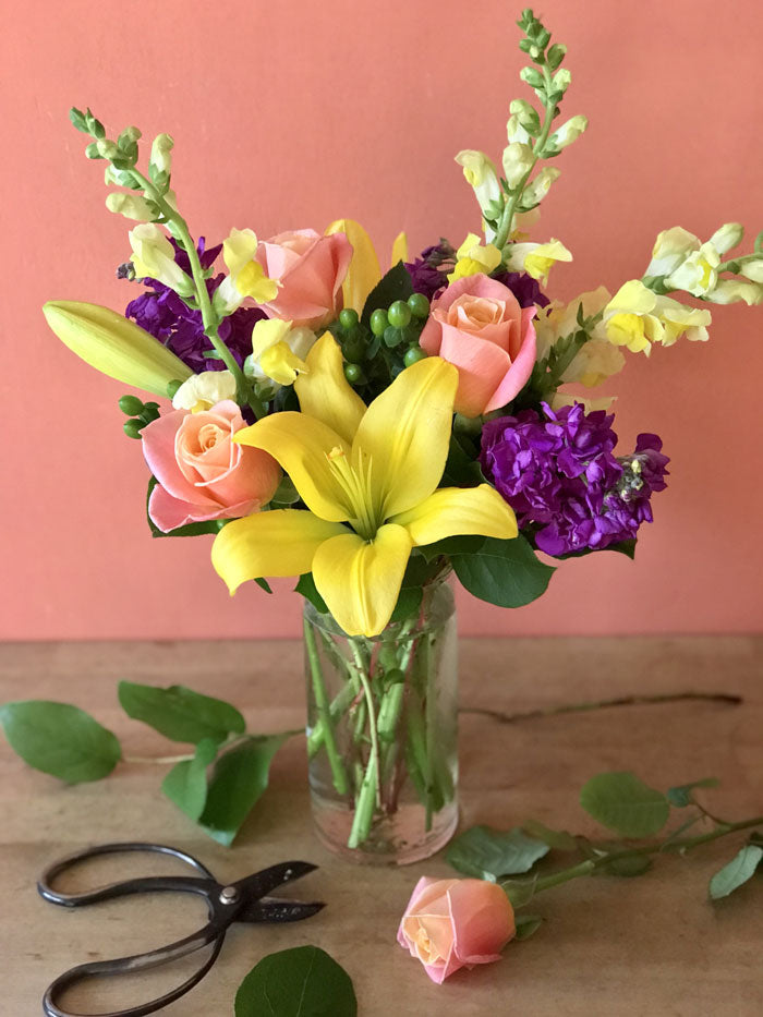 bright and colorful flower arrangement with yellow lilies, yellow snapdragons, peach roses, and purple stock
