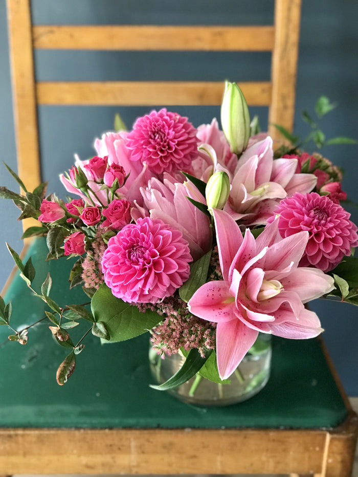pink rose lilies, hot pink dahlias an spray roses in a short glass cylinder vase