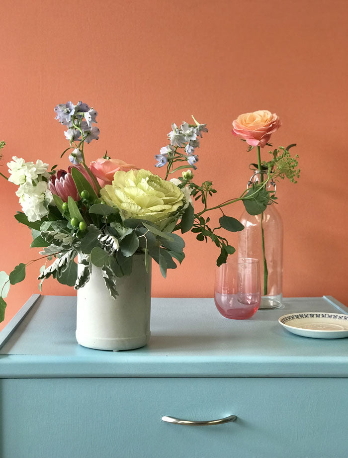 pink, blue, white, and green flower arrangement sitting on a blue end table with a peach background