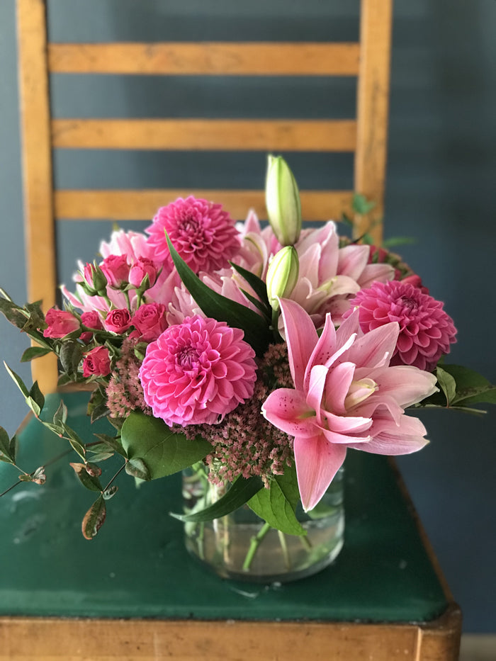 arrangement of hot pink dahlias, rose lilies, and spray roses in a glass vase