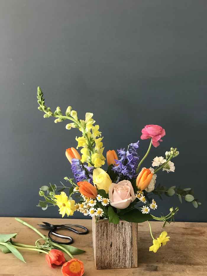 a reclaimed wood box filled with colorful spring flowers- tulips, hyacinth, ranunculus, stock, and snapdragons