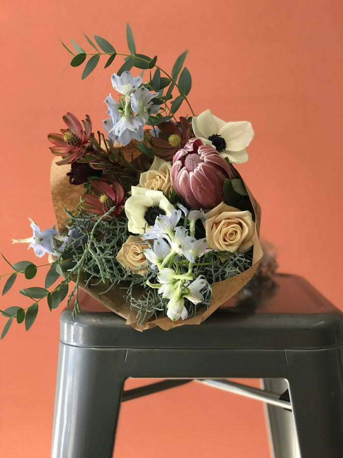 winter subscription bouquet with protea, anemone, and roses with tan roses